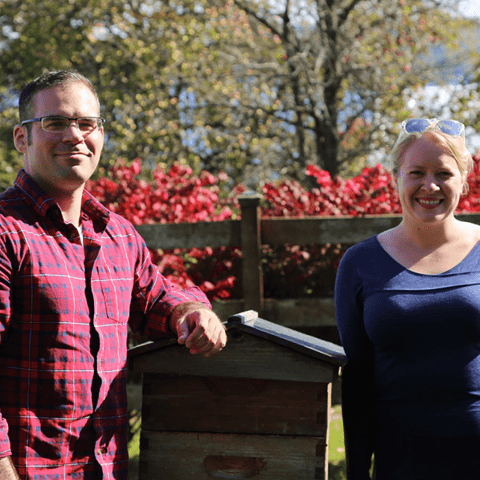 Nathan Oakes, CTO, and Hailey Scofield, CEO, of Combplex, stand next to bee hives at the Wegmans Organic Farm in 2019.