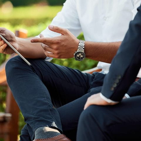 Two individuals hold a business meeting in a park. Their faces are not visible, but one holds a tablet in their hands.