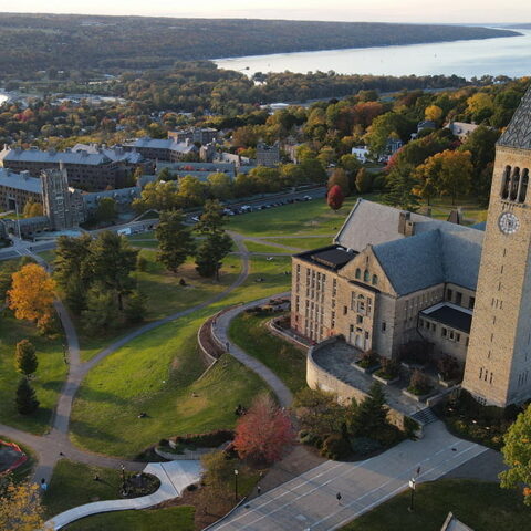 Overhead photo of Cornell campus and clock tower with Cayuga Lake in the background.