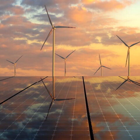 Wind turbines and solar panels against a sunset.