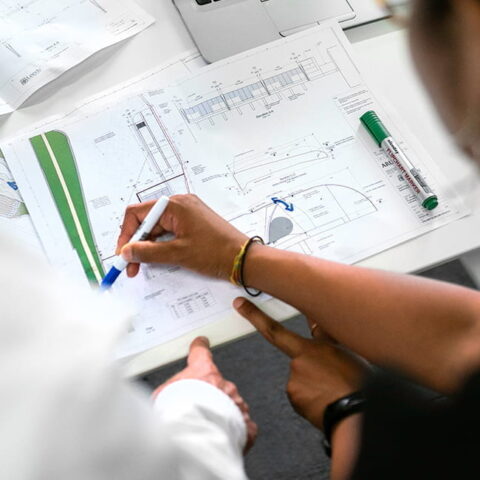Hands pointing at a paper with graphs and another hand with a marker drawing on the paper.