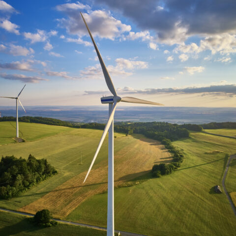 Close up of a wind turbine with more wind turbines in a field in the distance.