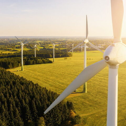 Close up of a wind turbine with more wind turbines in a field in the distance.